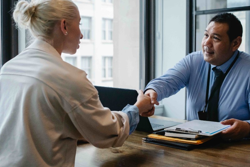 A recruiter offering a job to a candidate and shaking their hand to congratulate them.